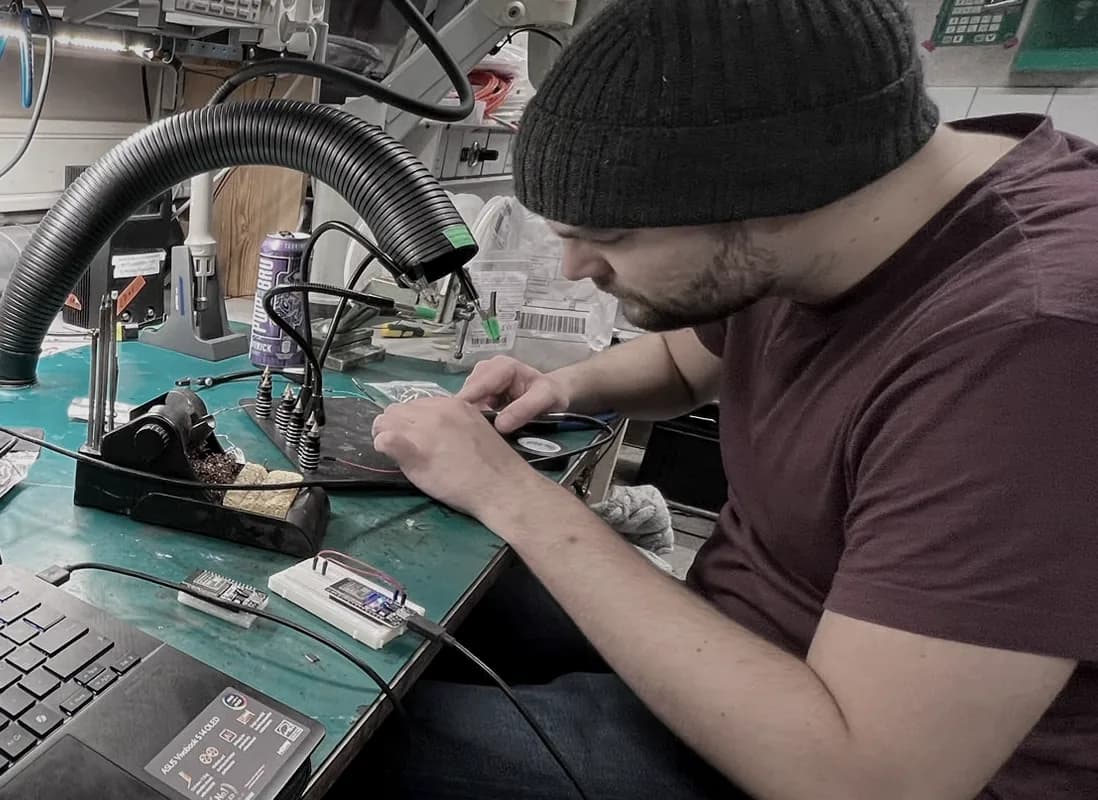 A co-founder soldering at the prototyping bench, surrounded by test equipment.
